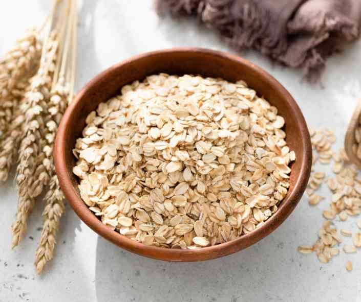 A wooden bowl of oats with oat sheafs next to it
