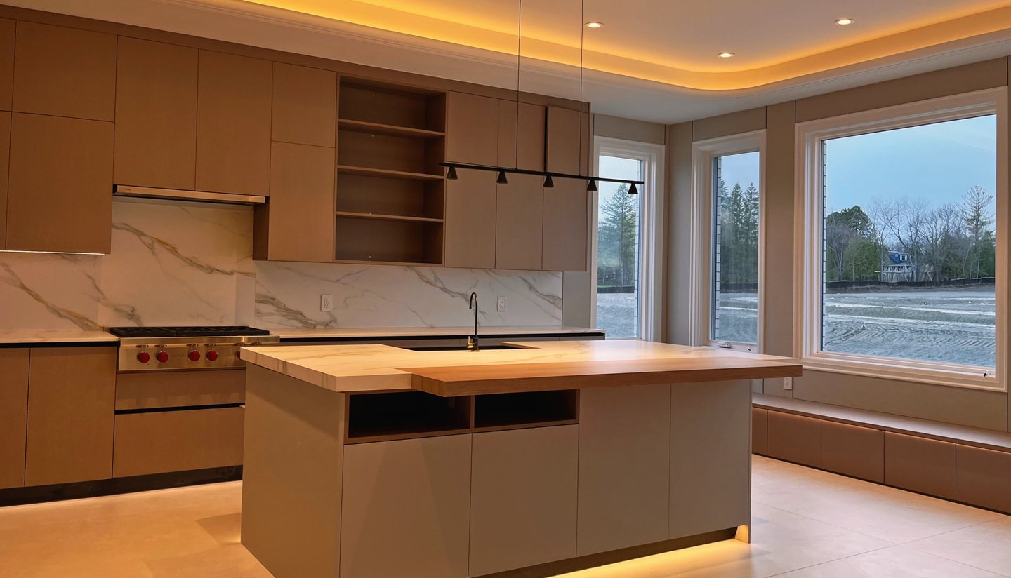 Modern luxury kitchen with wood cabinetry, a large marble island, and recessed warm ceiling lighting.