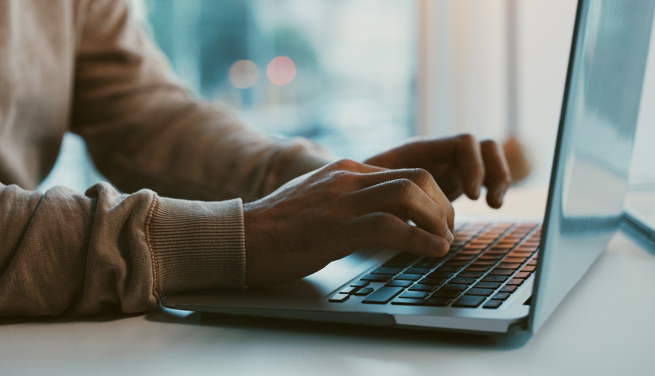 Person with beige sweater typing on a laptop symbolizing meaningful obituary services.