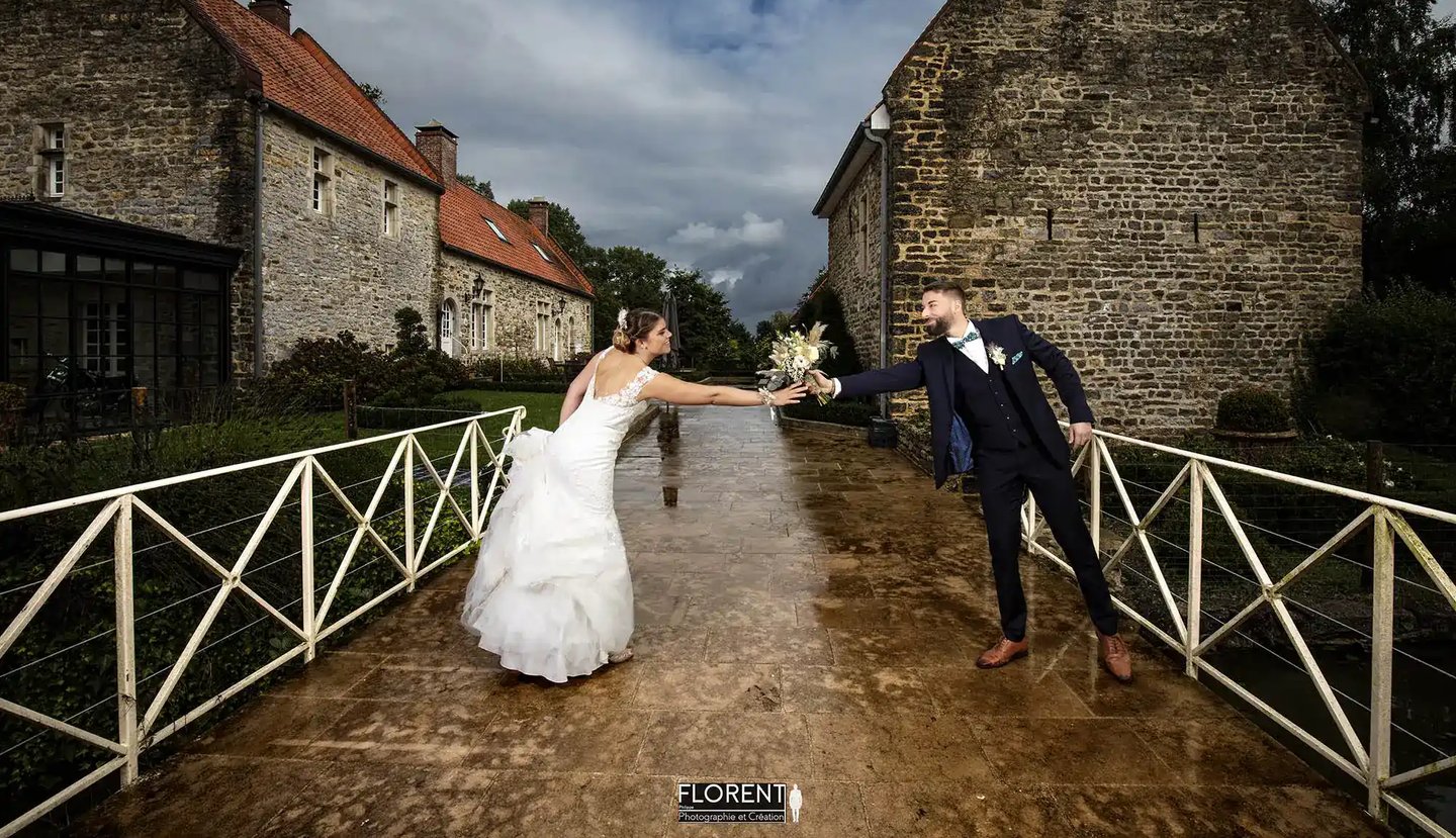 photographe mariage saint omer a bride and groom walking down a path in front of a stone building