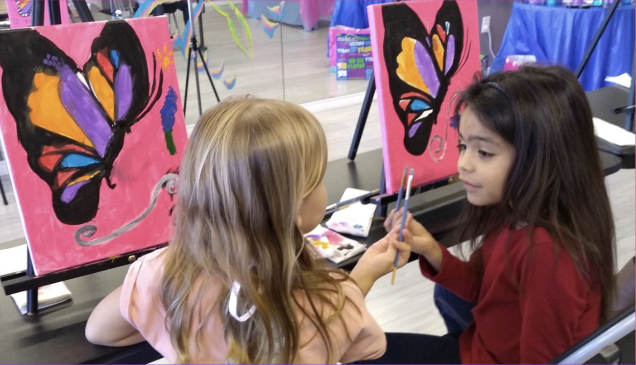 two little girls painting a butterfly on a canvas