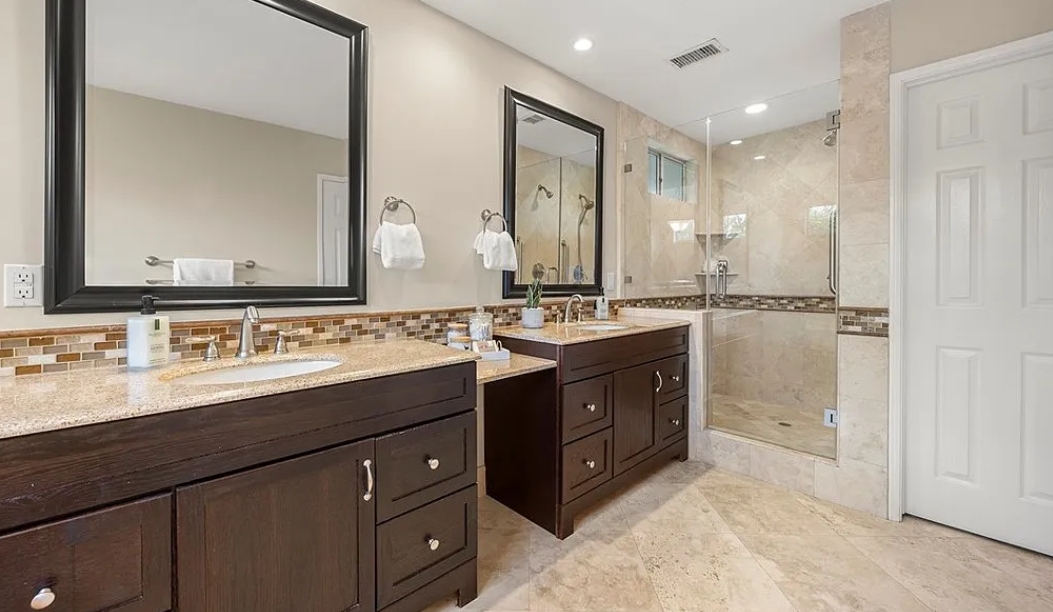 Bathroom remodel with a double vanity, framed mirrors, and stone countertops.