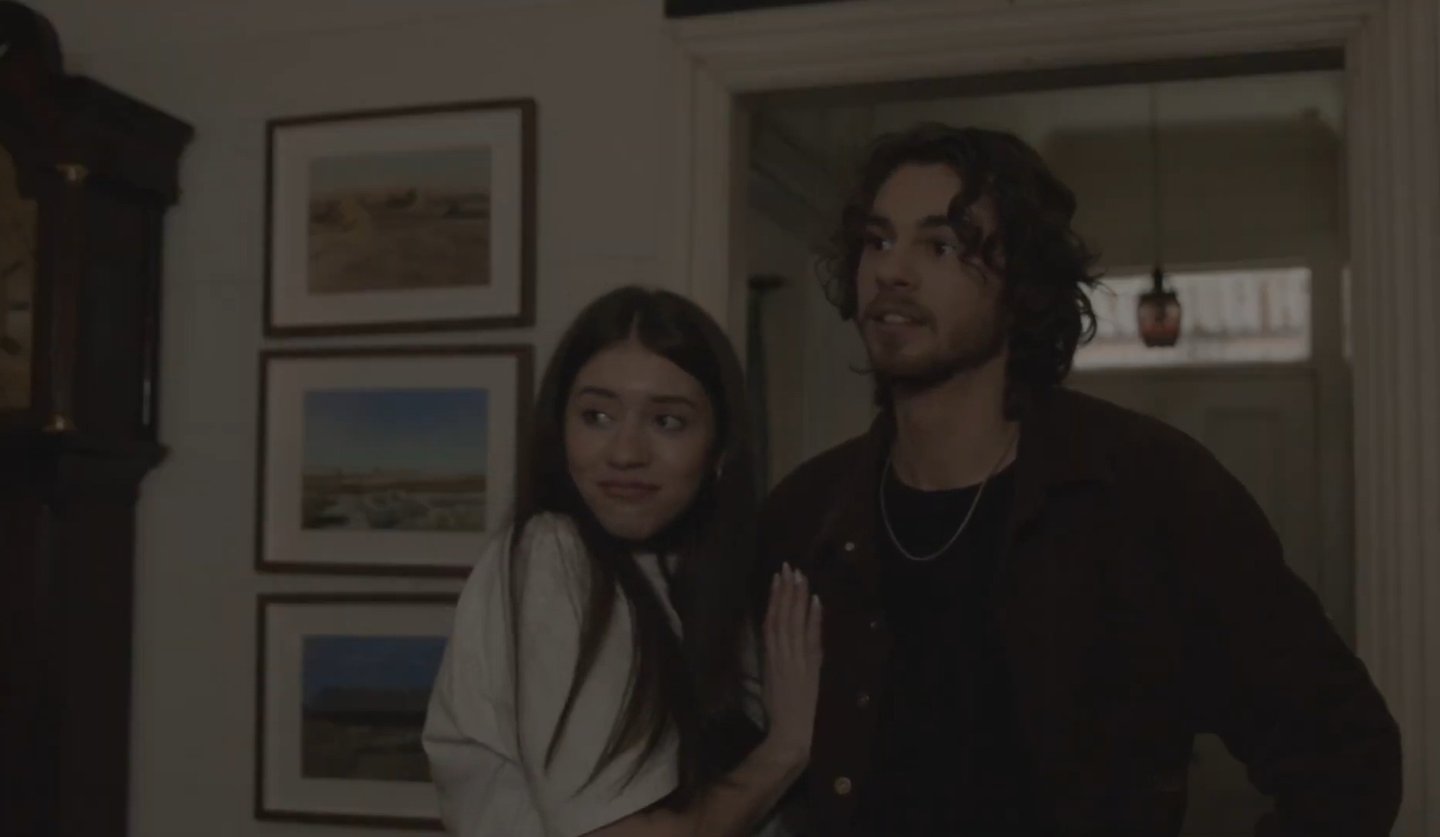 Young couple standing in a hallway, with framed art and a grandfather clock.