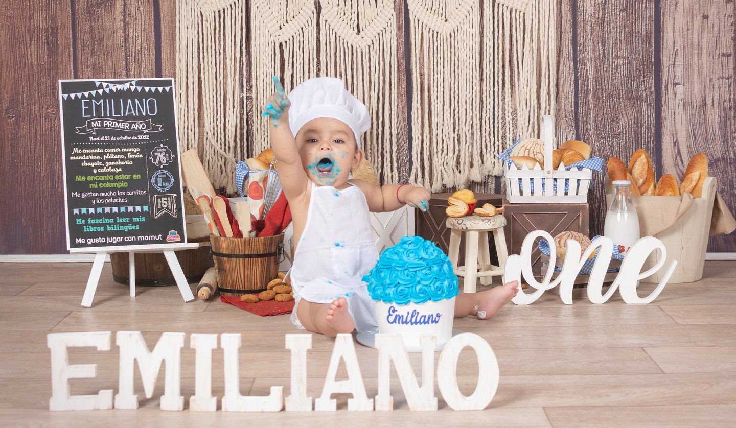 a baby boy in a white dress and a cake