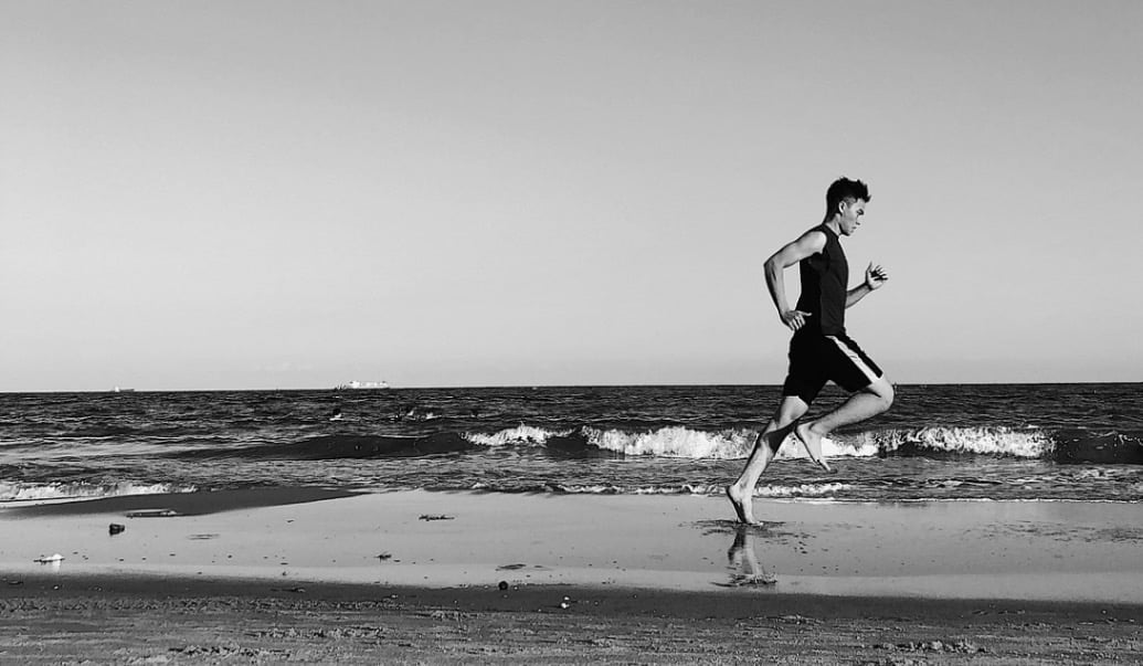 a man running on the beach with a surfboard