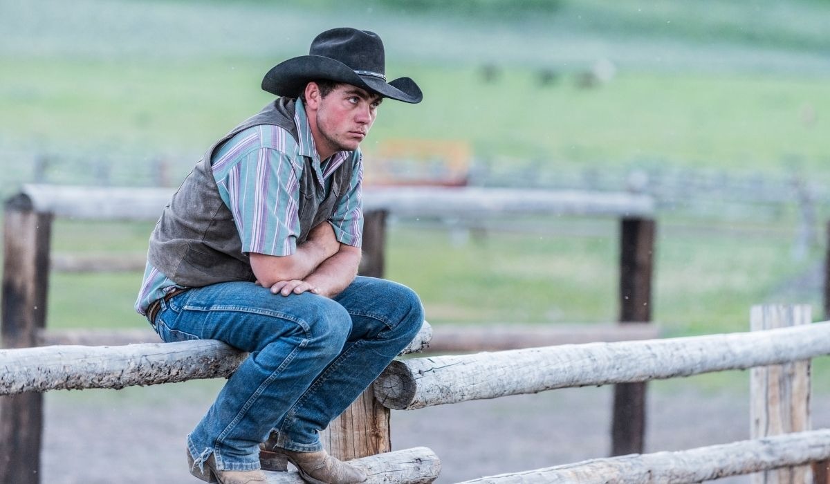 cowboy sitting on wood fence
