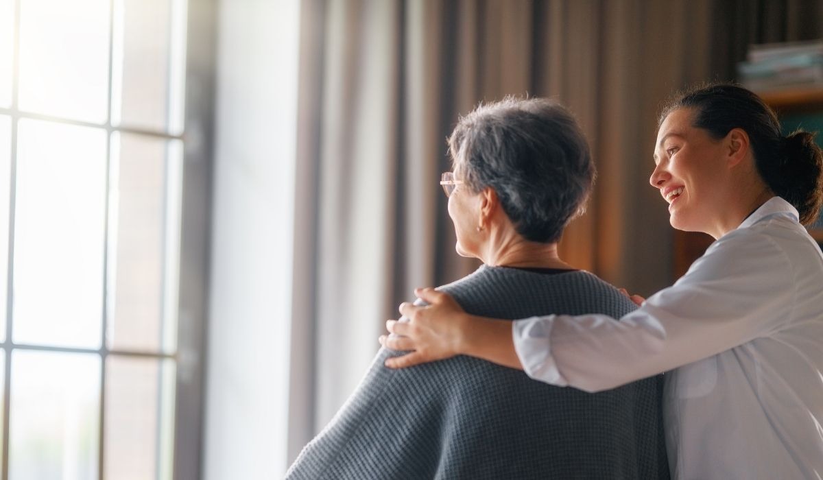 elderly woman looking out window next to nurse