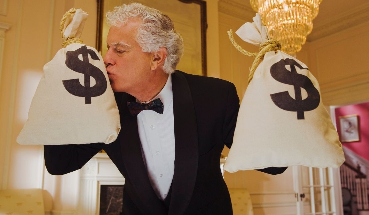 man in tuxedo kissing bags of money