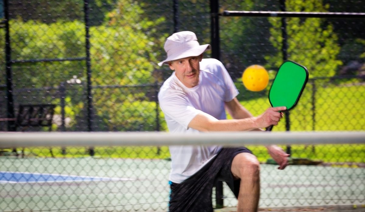 senior man with hat on playing pickleball