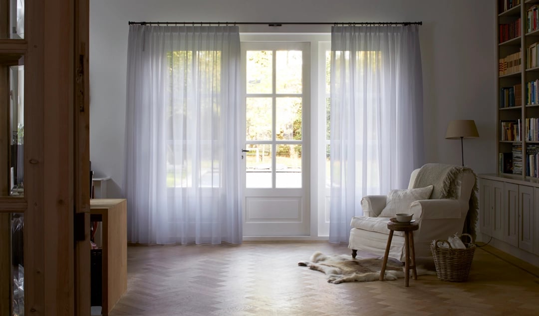Grands rideaux tamisants blanc devant de larges fenêtres dans une entrée avec fauteuil et tapis