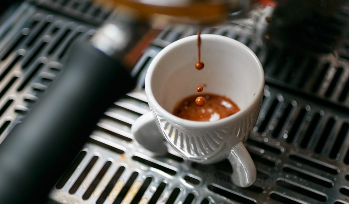 Fresh espresso dripping from a professional coffee machine into a white ceramic cup.
