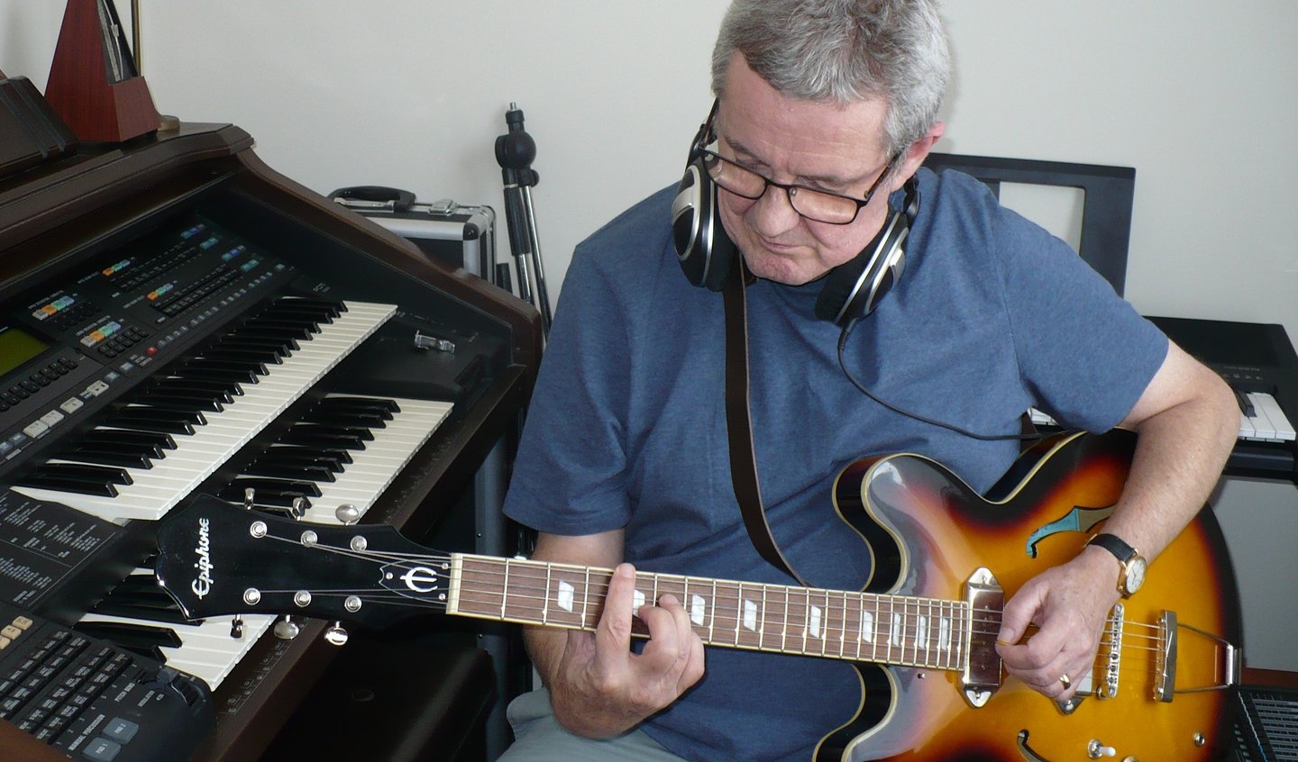 photograph of Julian Sumner with guitar and keyboards in recording studio