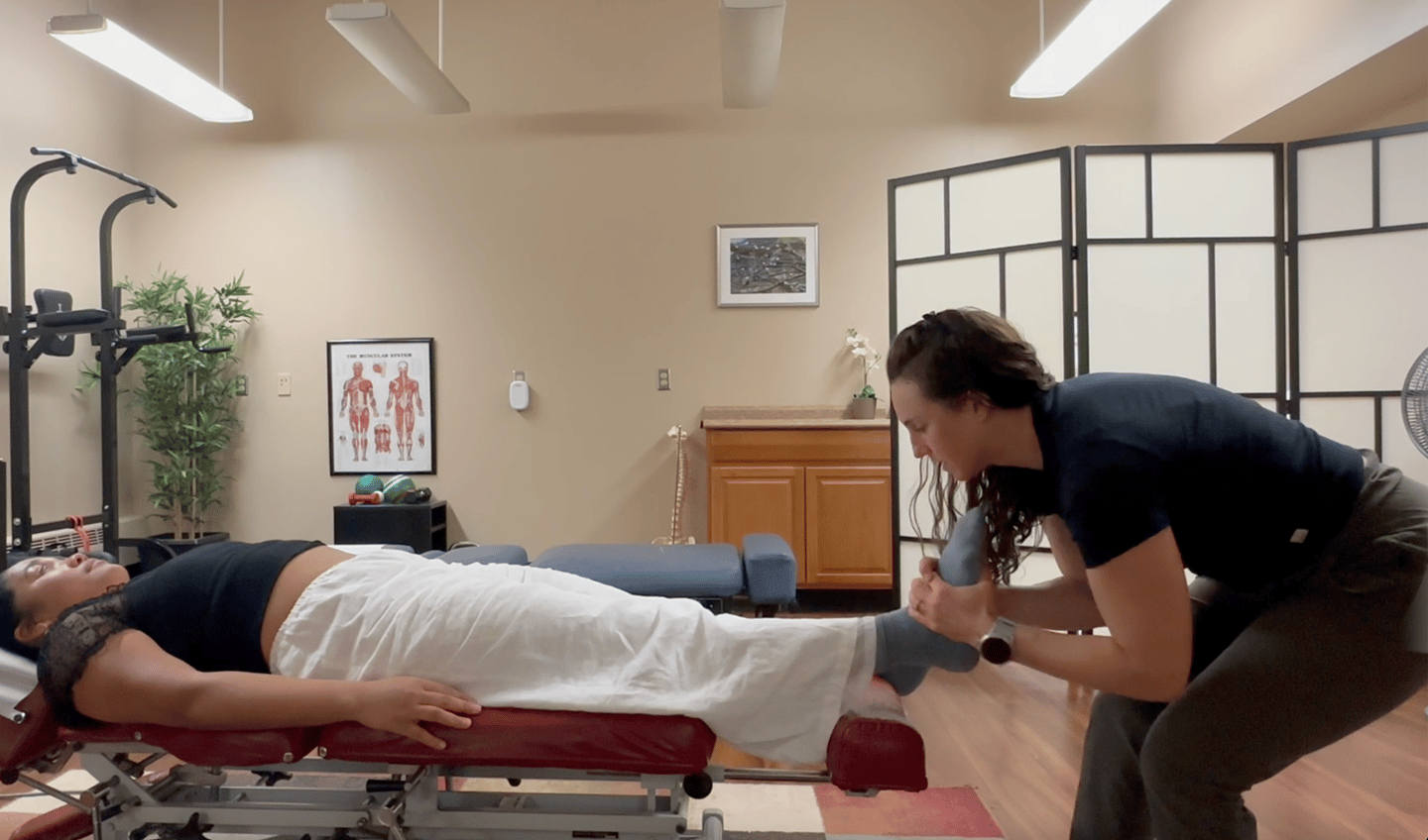 Chiropractor adjusting patient's foot while patient lays on back on chiropractic table. 
