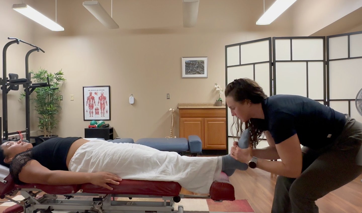Chiropractor adjusting patient's foot while patient lays on back on chiropractic table. 