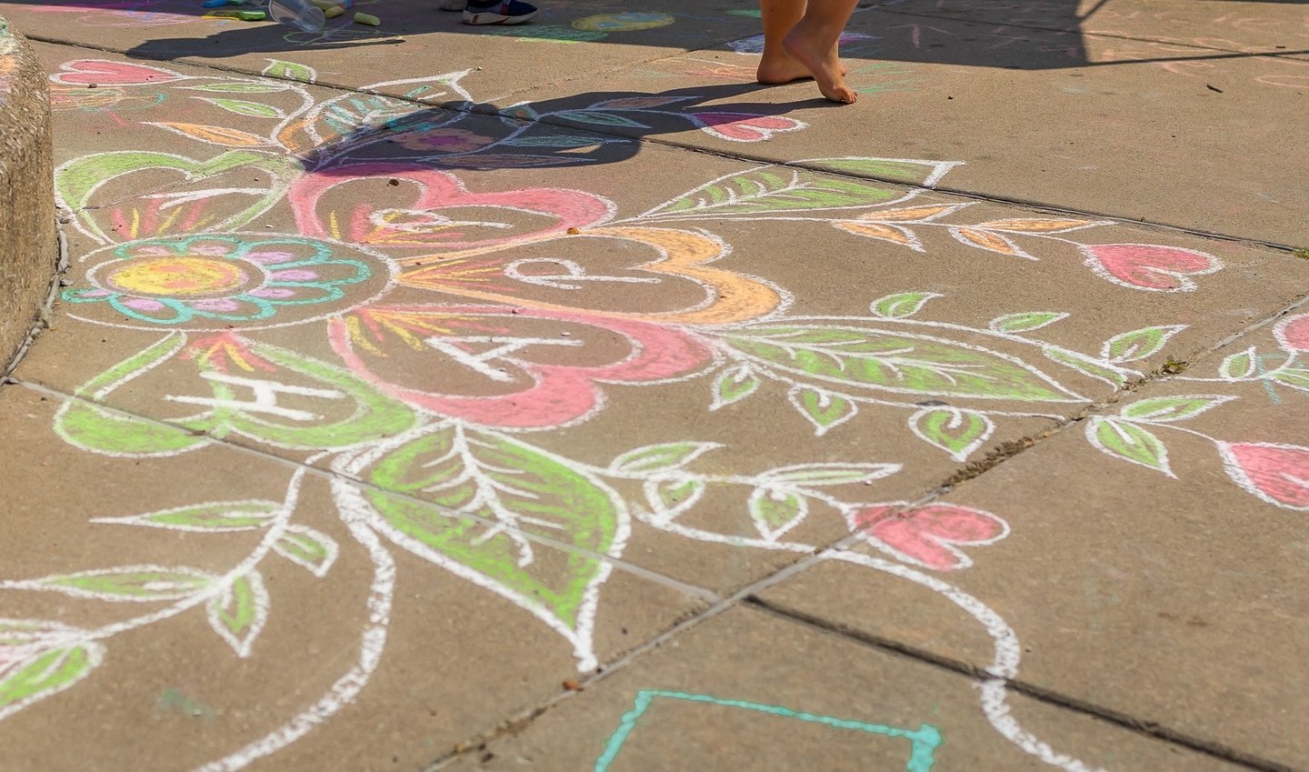 Colorful sidewalk chalk art featuring a large floral design with hearts and leaves on a concrete path.