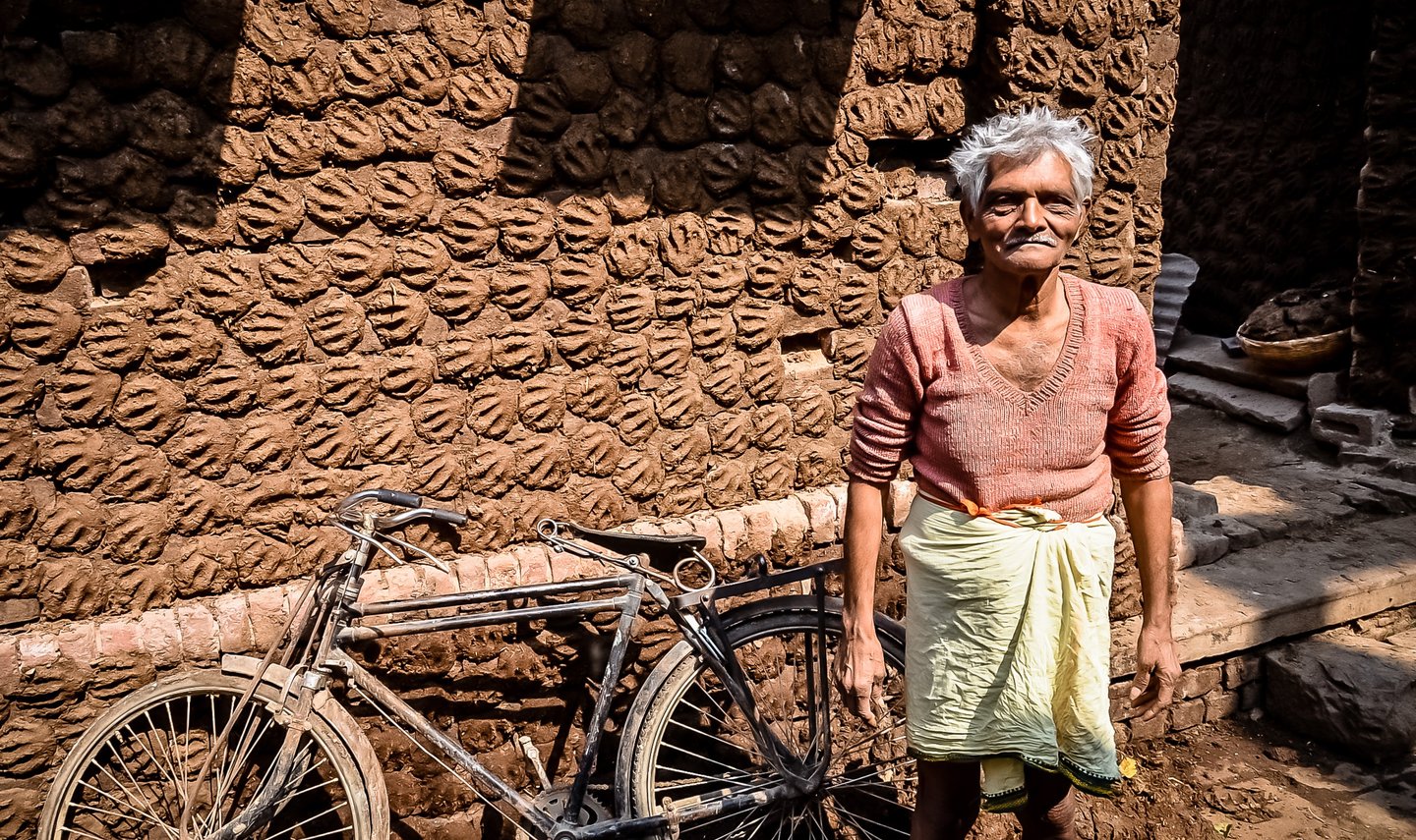 Showing his work of cow dung paddies for fuel drying in the sun against a wall in Varanasi, India.