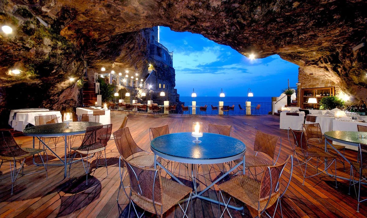 Luxury fine dining restaurant inside a coastal sea cave overlooking the blue ocean at twilight.