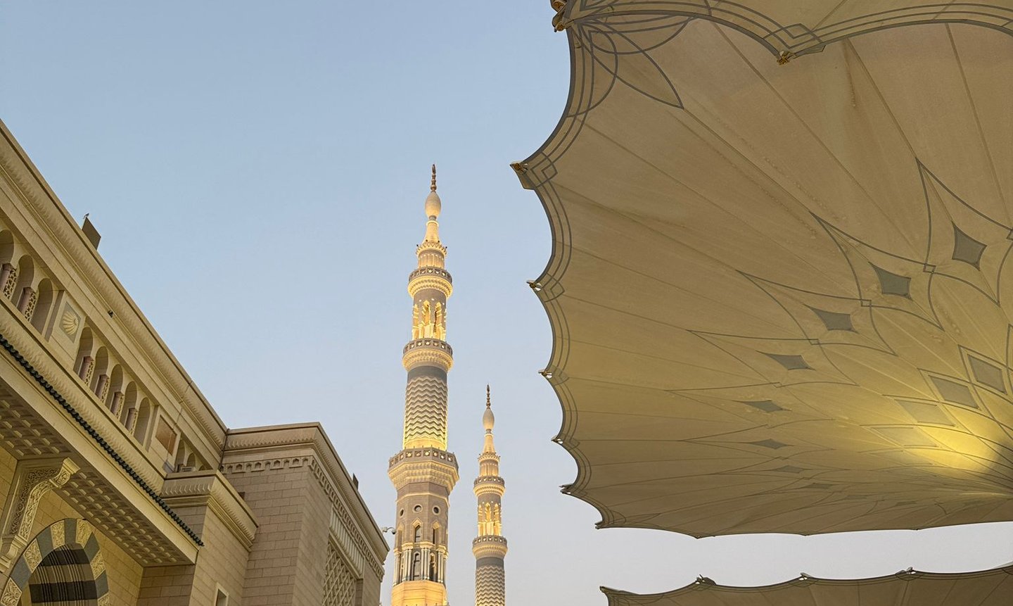 Illuminated minarets of Al-Masjid an-Nabawi in Medina beneath large white umbrellas at dusk.