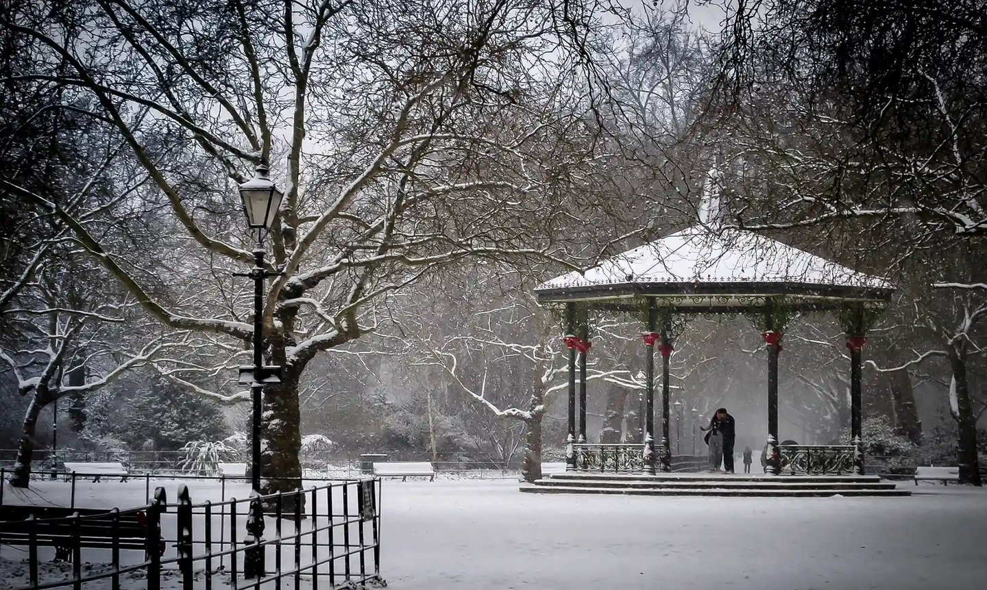 A scenic snowy park landscape featuring a traditional Victorian bandstand and bare winter trees.