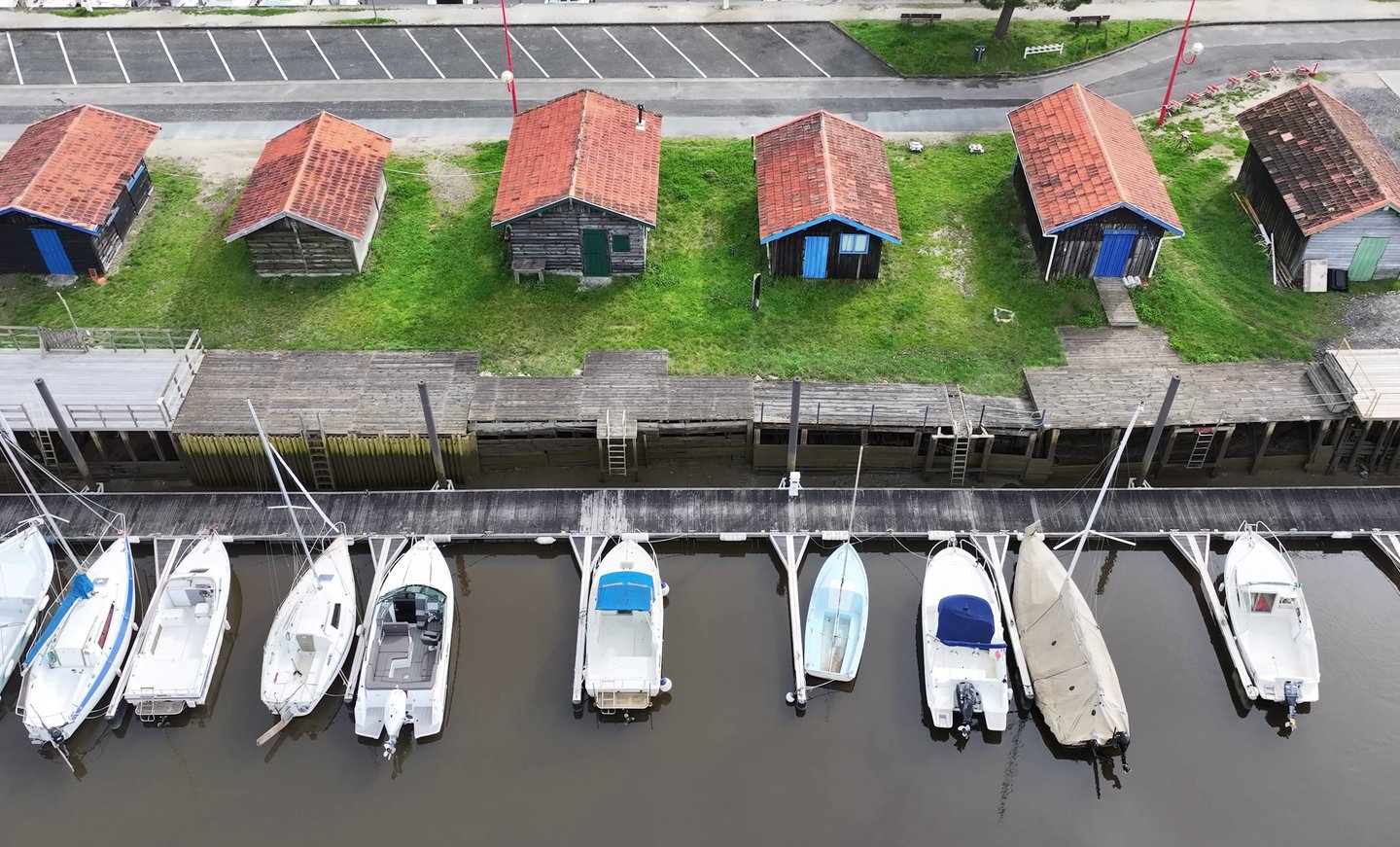 Vue aérienne de cabanes à huîtres colorées et de bateaux blancs amarrés sur un quai de la marina