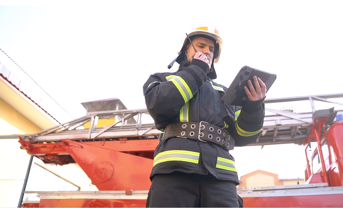 Firefighter speaking on a PoC radio and looking at information on a tablet