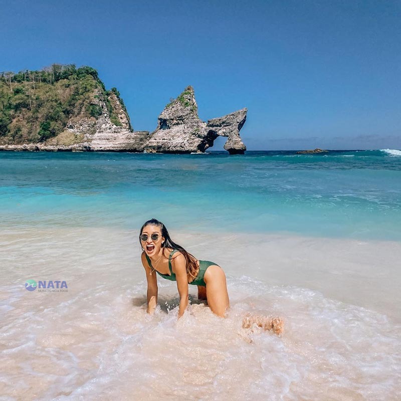A woman in a green swimsuit poses on Atuh Beach in Nusa Penida near the iconic rock formations.
