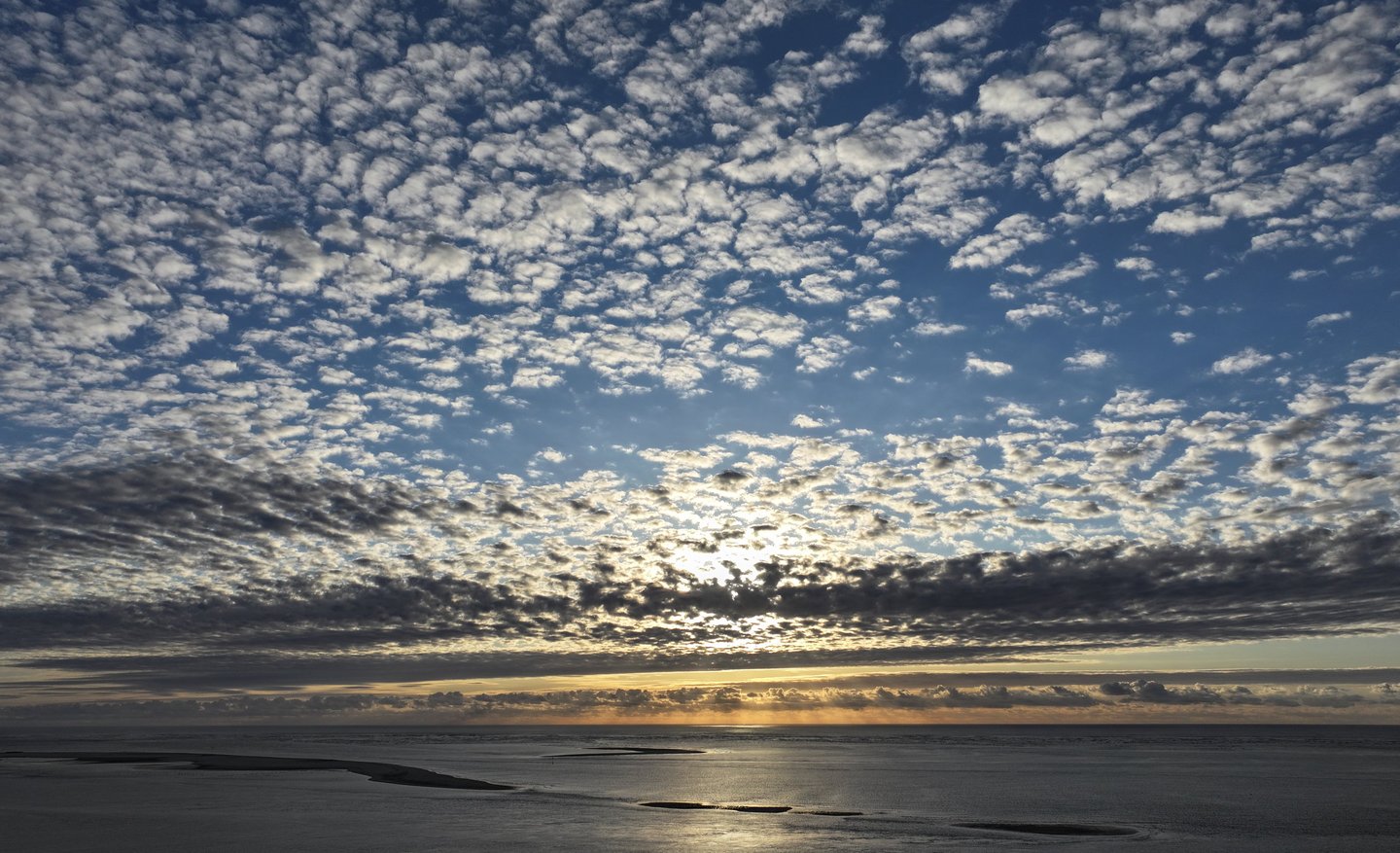 Coucher de soleil grand-angle sur un océan calme avec des formations nuageuses spectaculaires