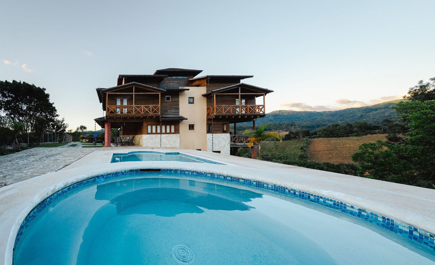 una villa de madera con piscina y una casa grande al fondo