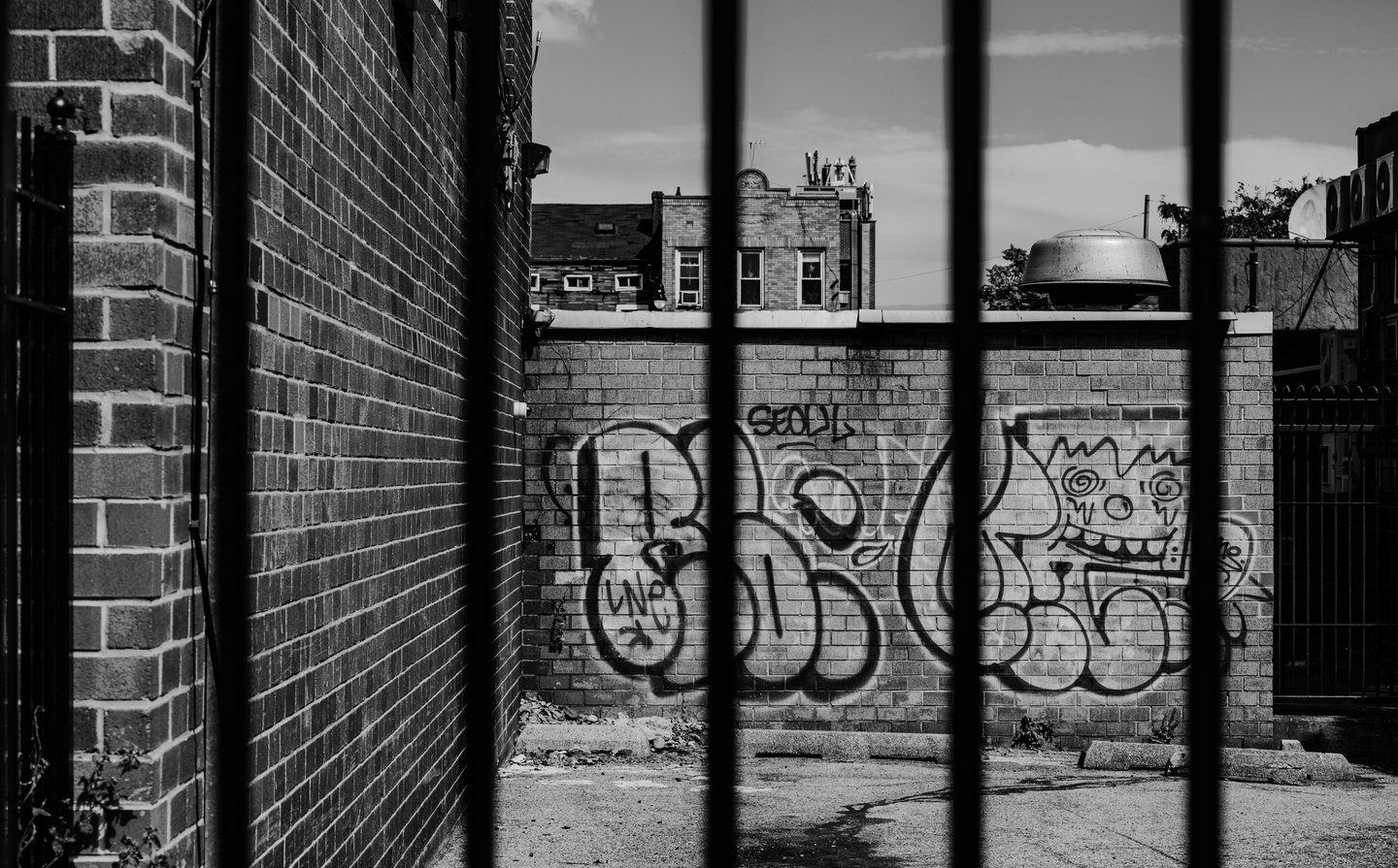 a blurred fence with a graffiti wall in the background on a brooklyn street