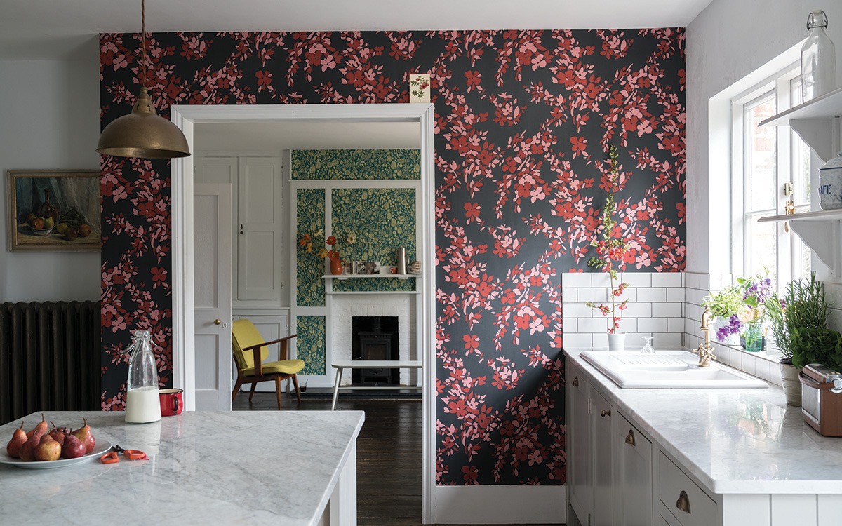 Modern kitchen with red floral wallpaper, marble countertops, and a view into a cozy living room.