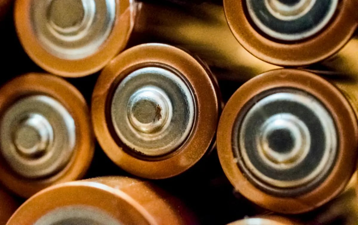 Close-up top view of several copper and gold alkaline AA batteries showing the positive terminals.