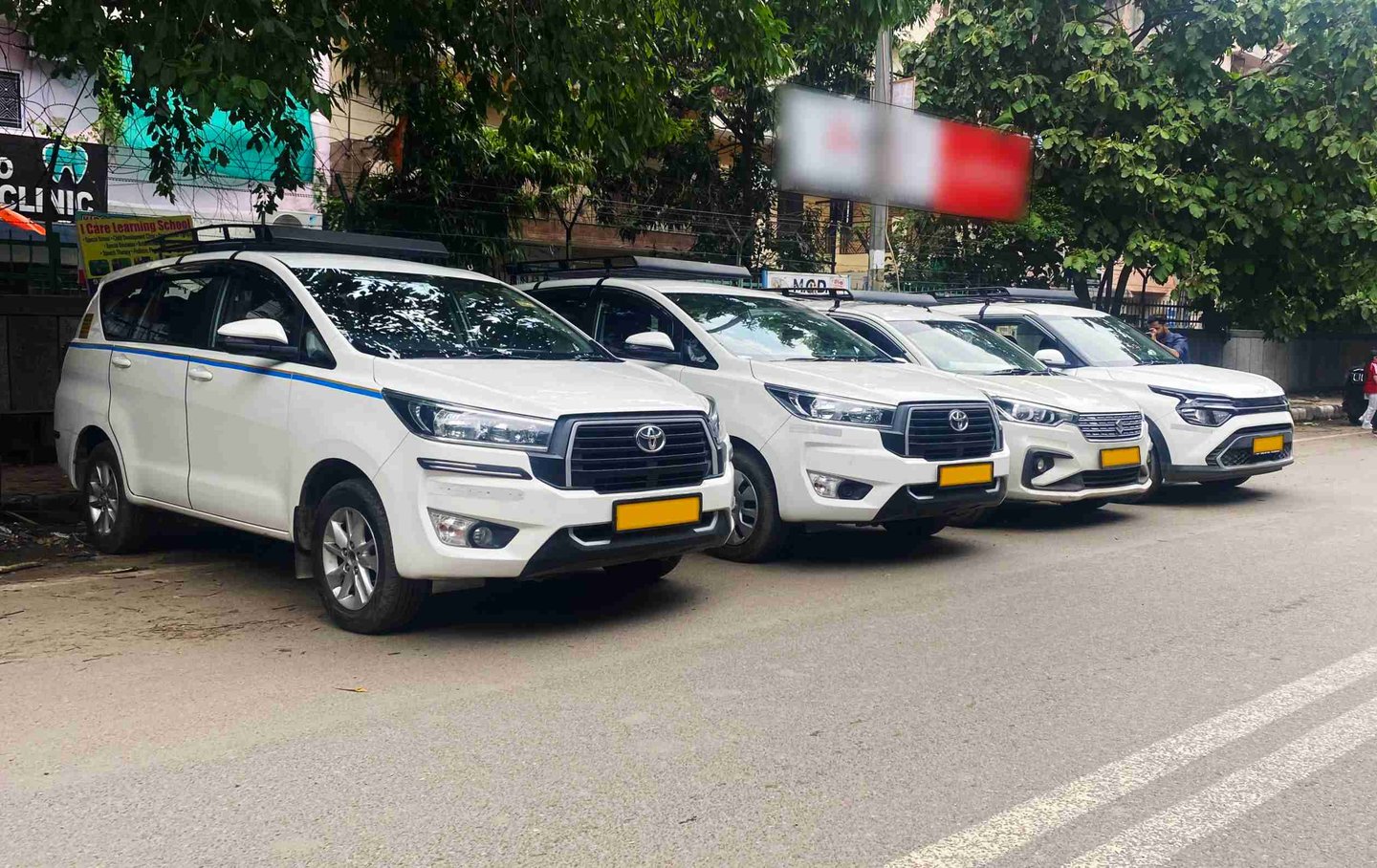 A row of white Toyota Innova Crysta taxis parked on a city street for commercial rental services.