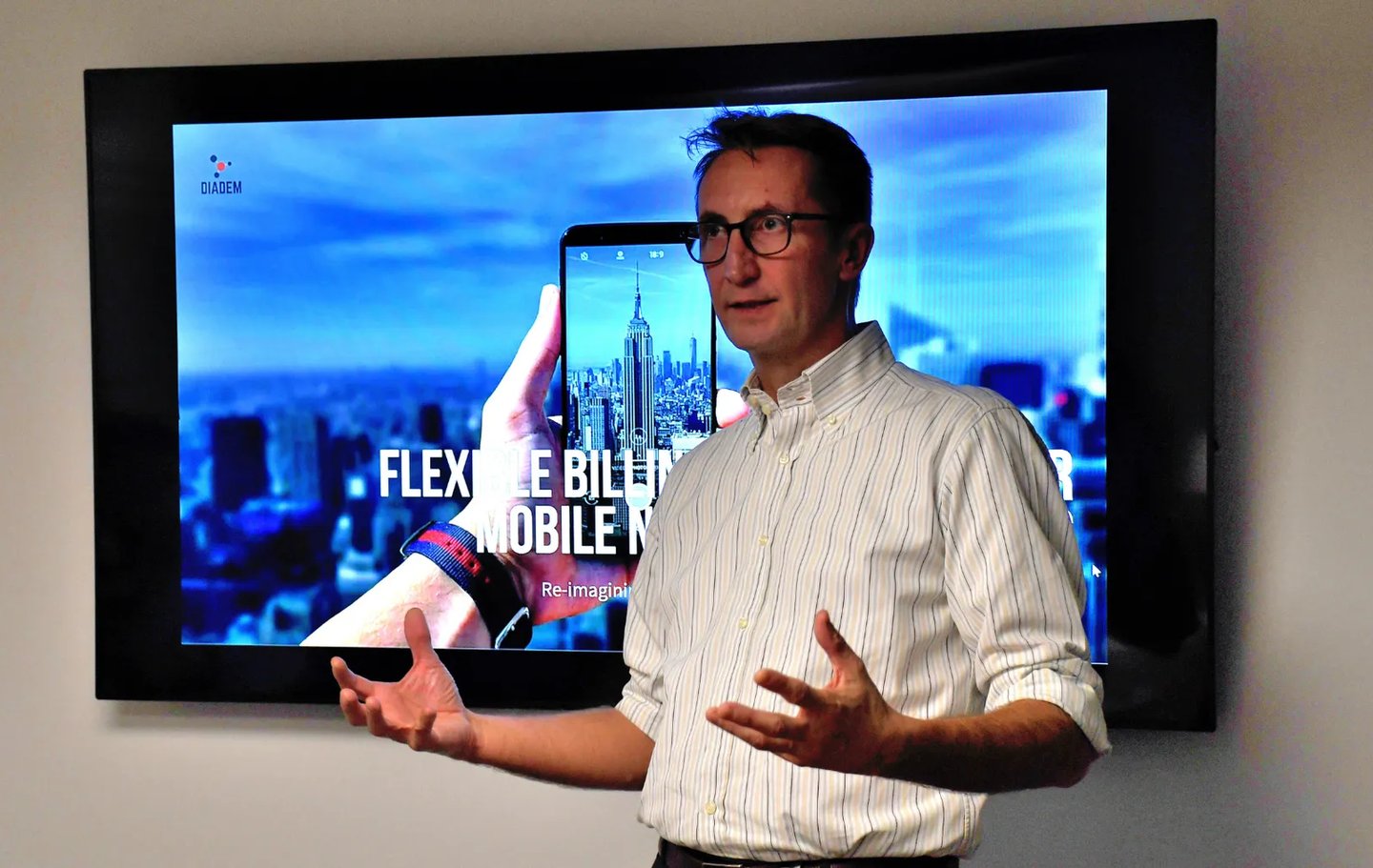 a man standing in front of an audience with a tv in the background