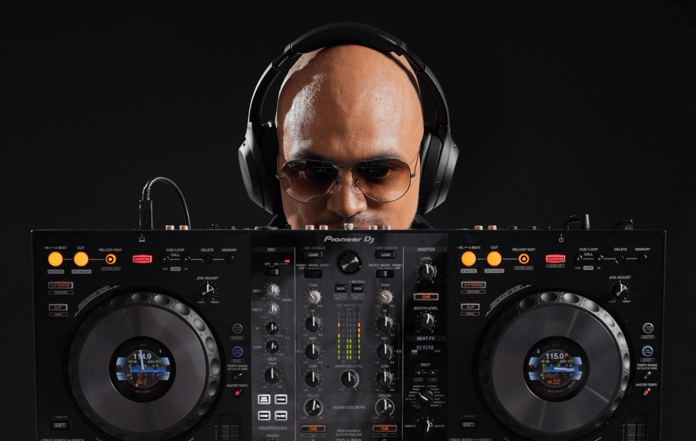 a man in a white suit, sunglasses and headphones holding a DJ controller