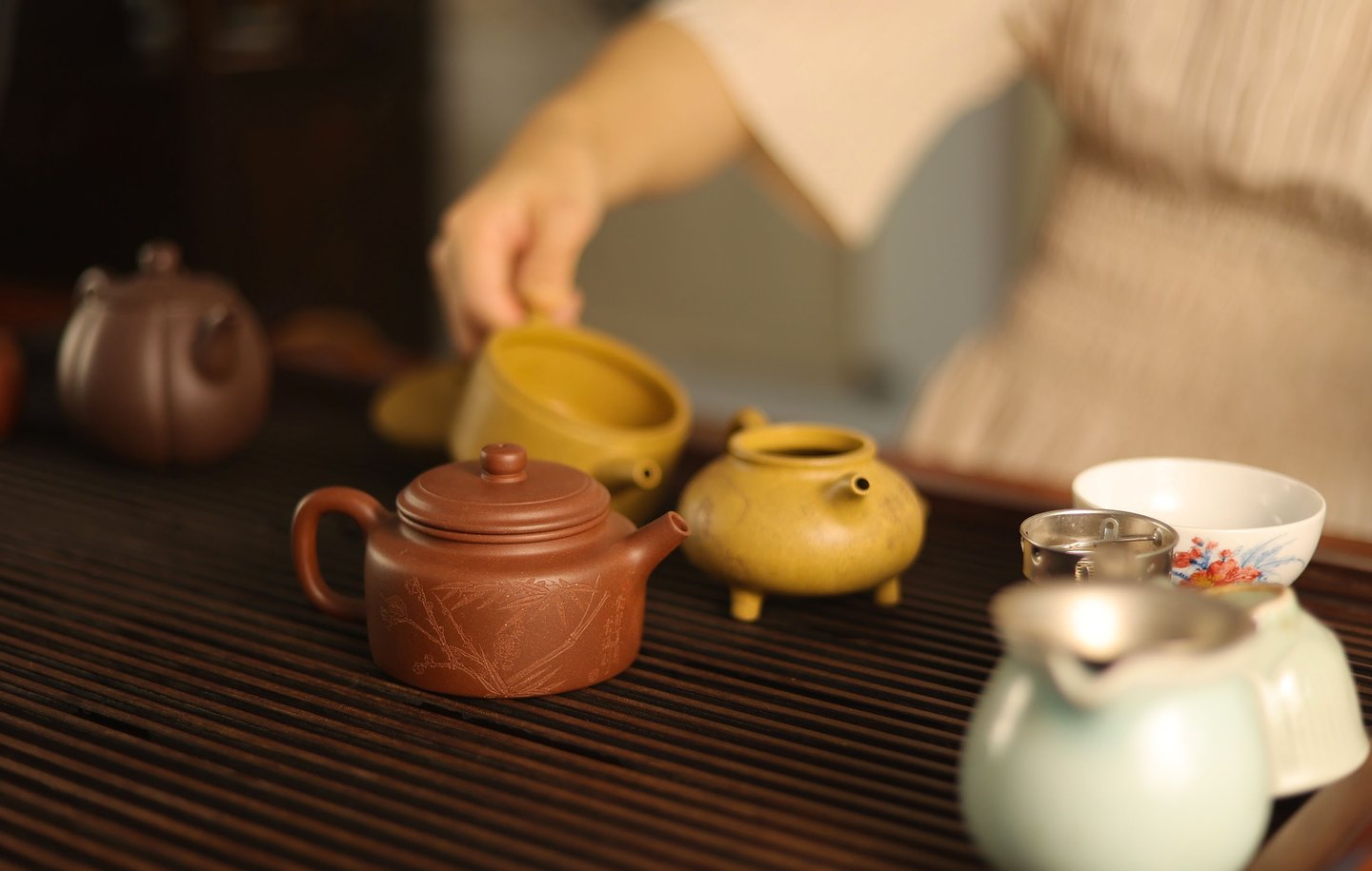 Person pouring water from a teapot with cups and a tea strainer on a wooden table