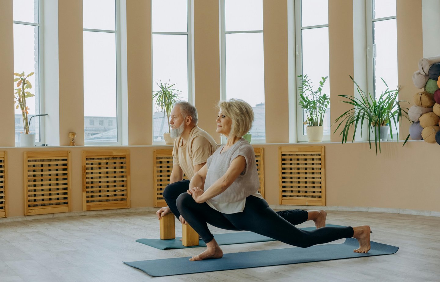 Active senior couple practicing yoga lunges on mats in a bright wellness studio.