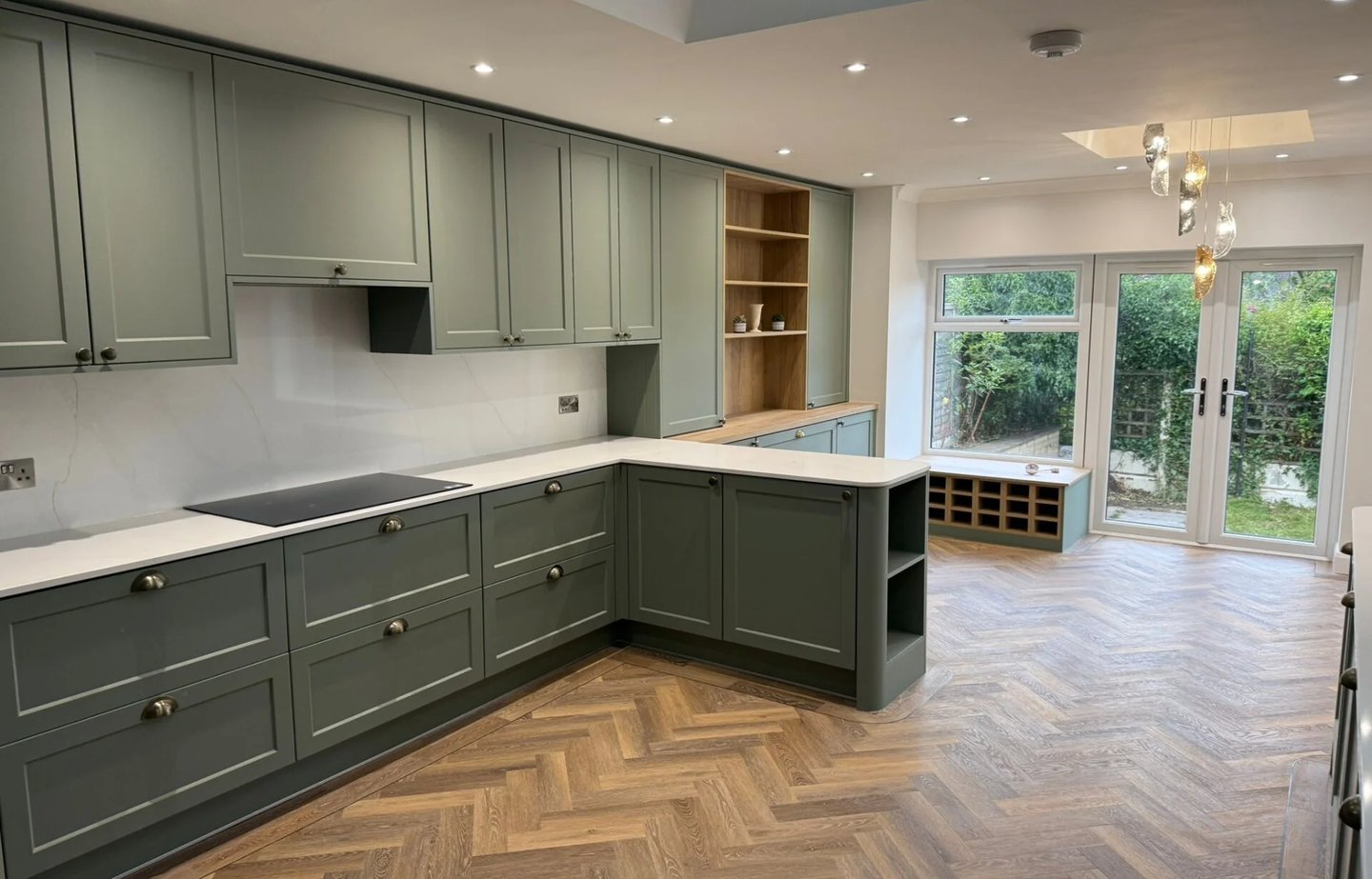 Modern sage green shaker kitchen with white quartz countertops and oak herringbone flooring.