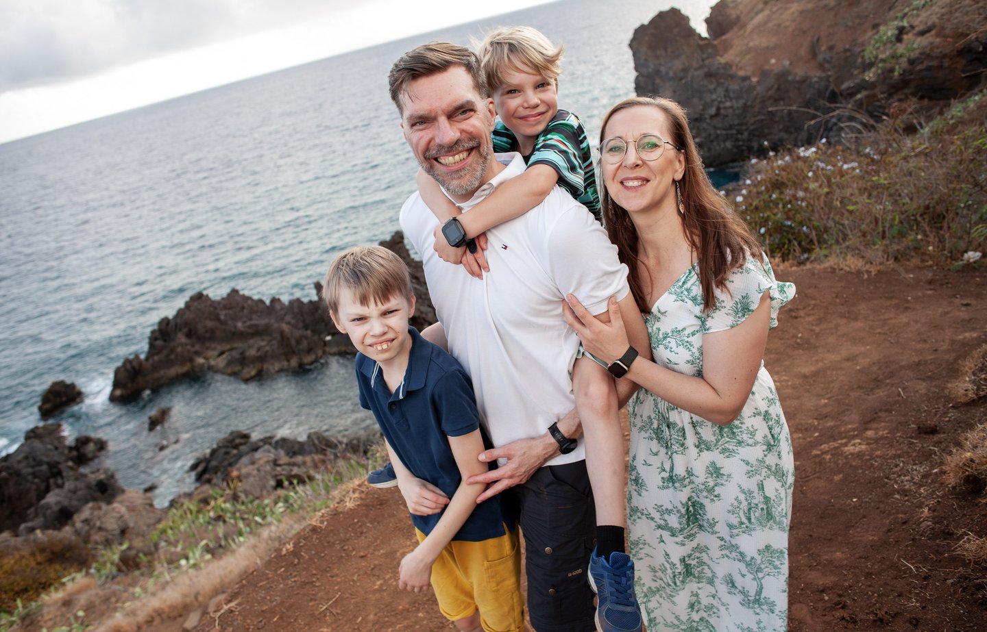 Smiling family poses together on Lido cliffs above Atlantic Ocean at Madeira, lifestyle travel and natural coastal scenery.