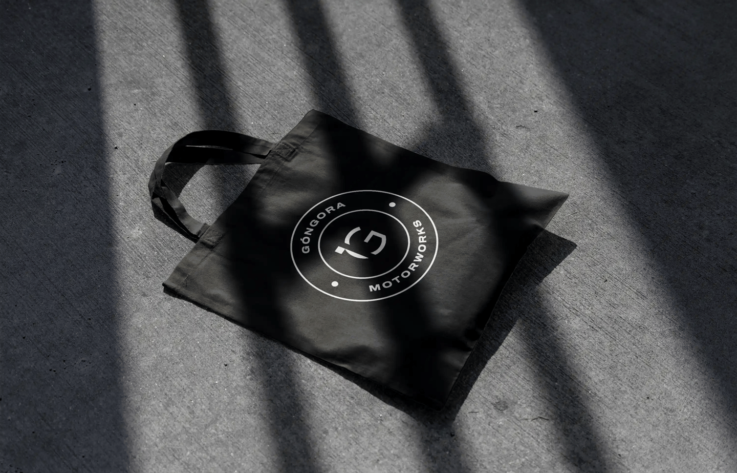 Totebag negra sobre el asfalto con el logo de Góngora Motorworks en blanco