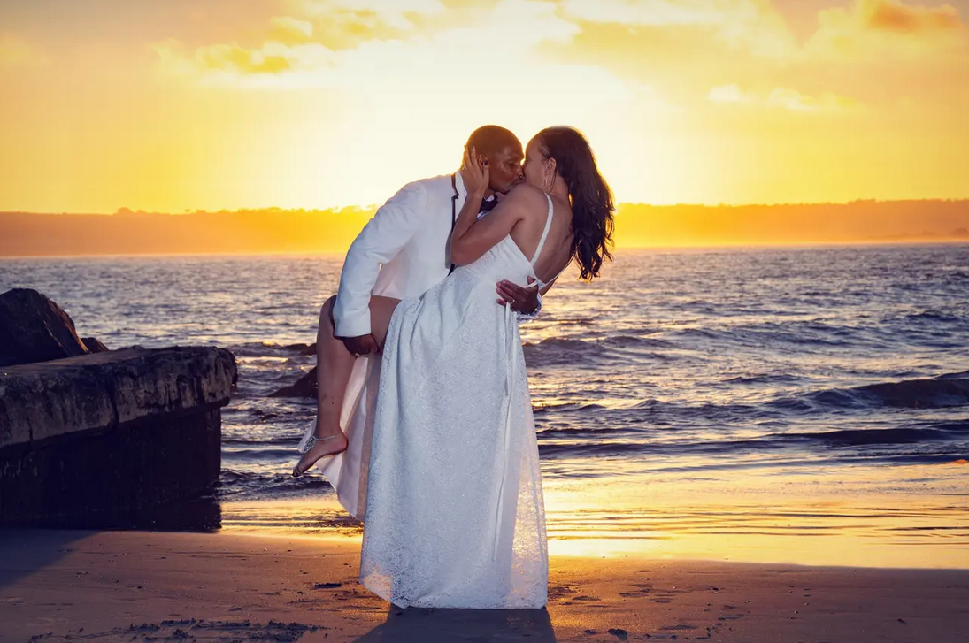 black bride and groom kissing on beach with golden sunset