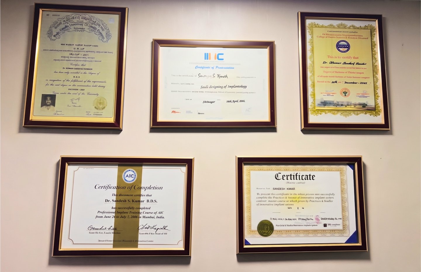 Professional dental certificates and implantology diplomas framed on a clinic wall for Dr. Sandesh Kumar.