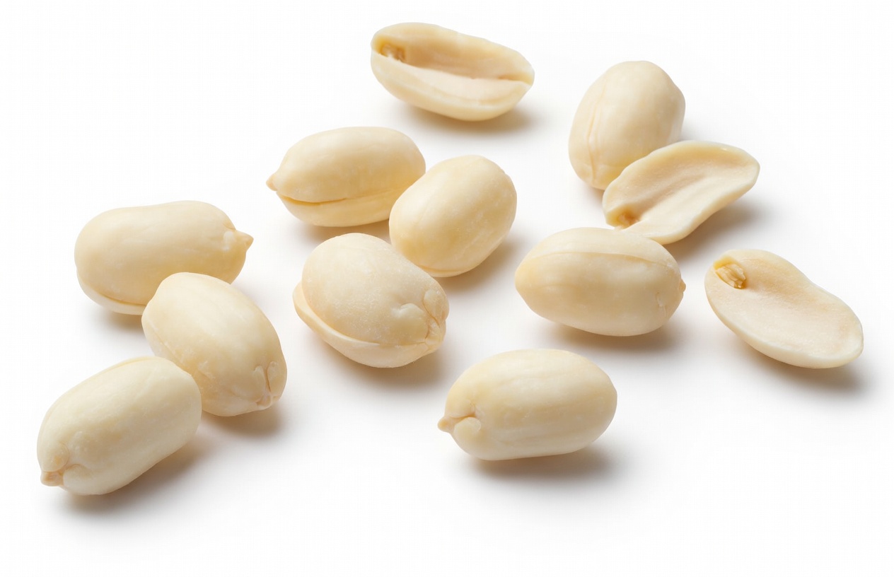 A collection of raw, blanched peanuts without shells scattered on a clean white background.