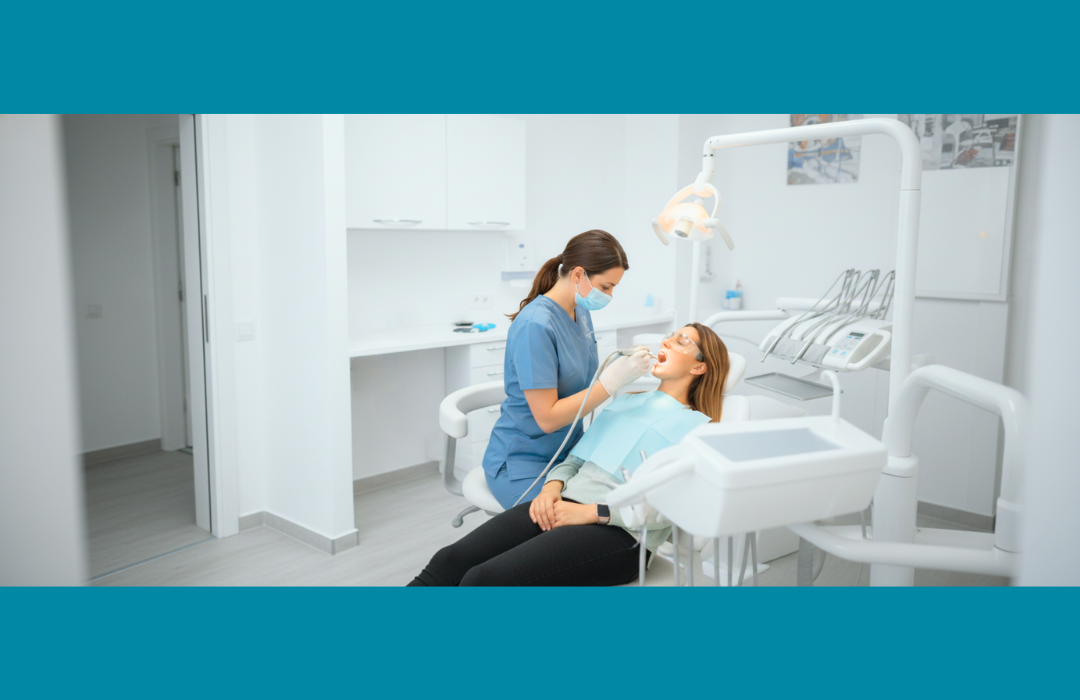 Una dentista con mascarilla y uniforme azul examinando la boca de una paciente 