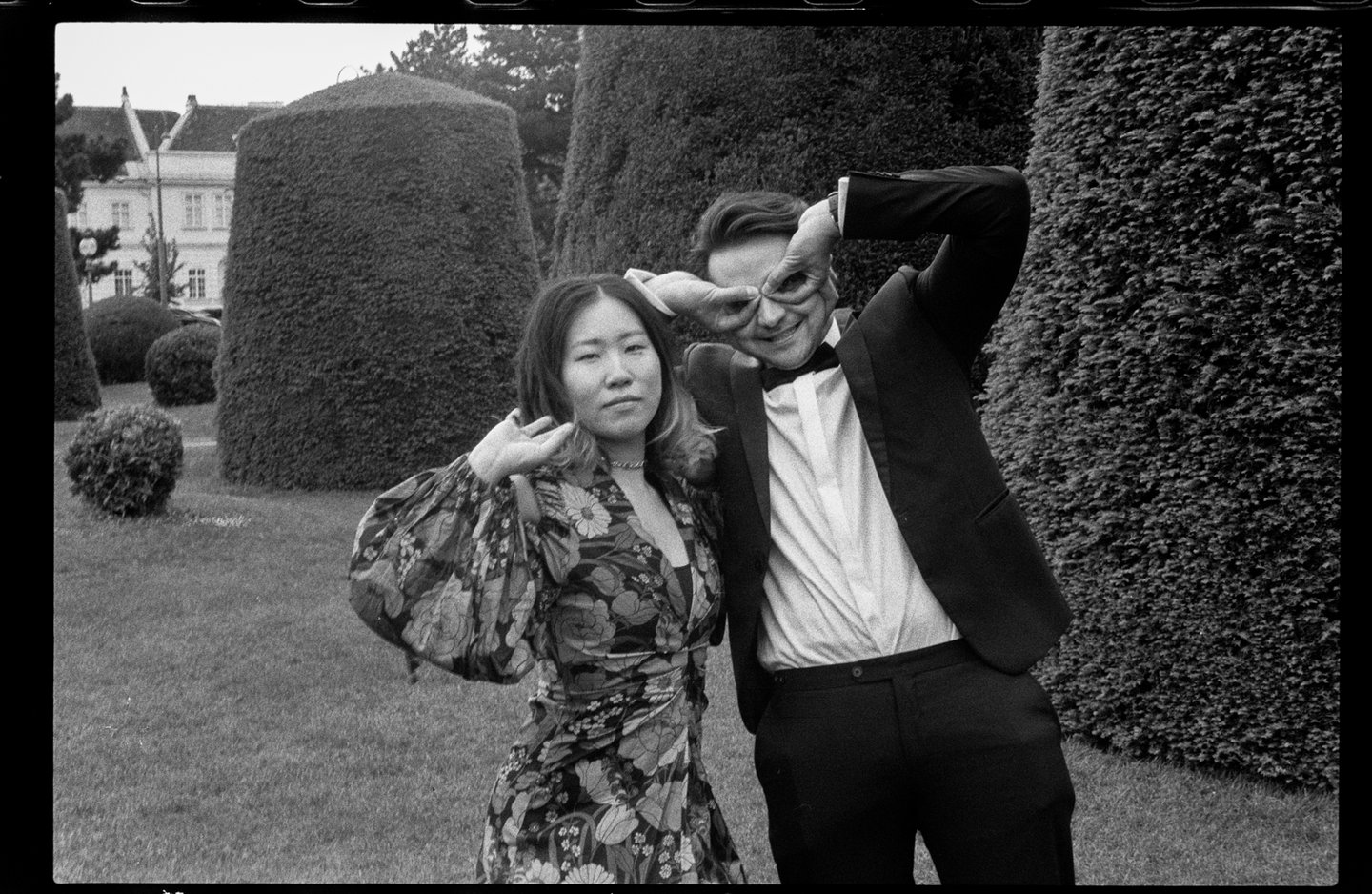 Couple wearing party clothes in a park posing quirky. B&W film photo.