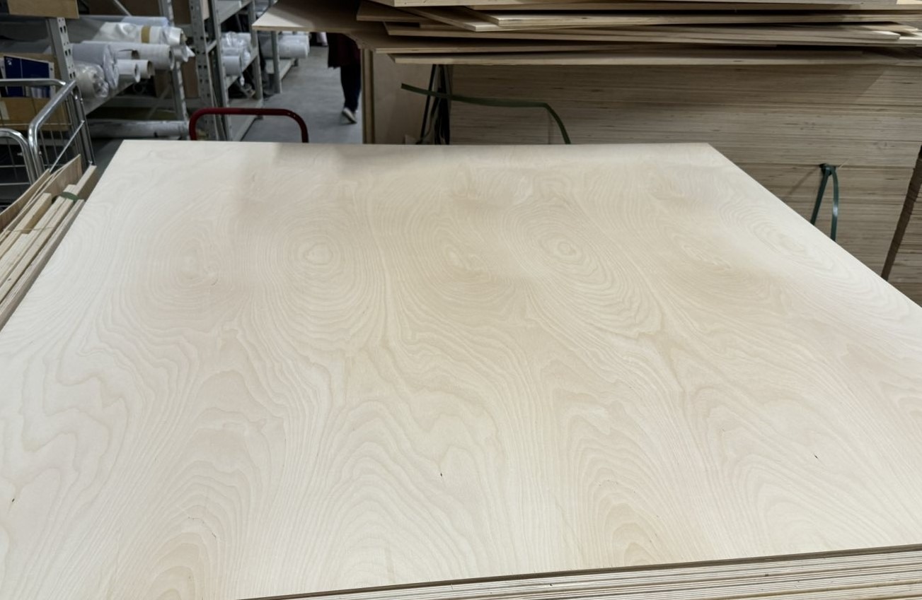 Close-up of a smooth birch plywood sheet with visible wood grain in a lumber warehouse.