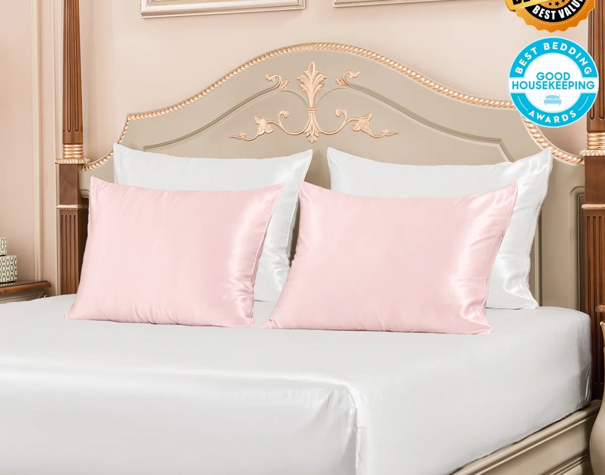 Luxury pink silk pillowcases on a white bed with an ornate wooden headboard.