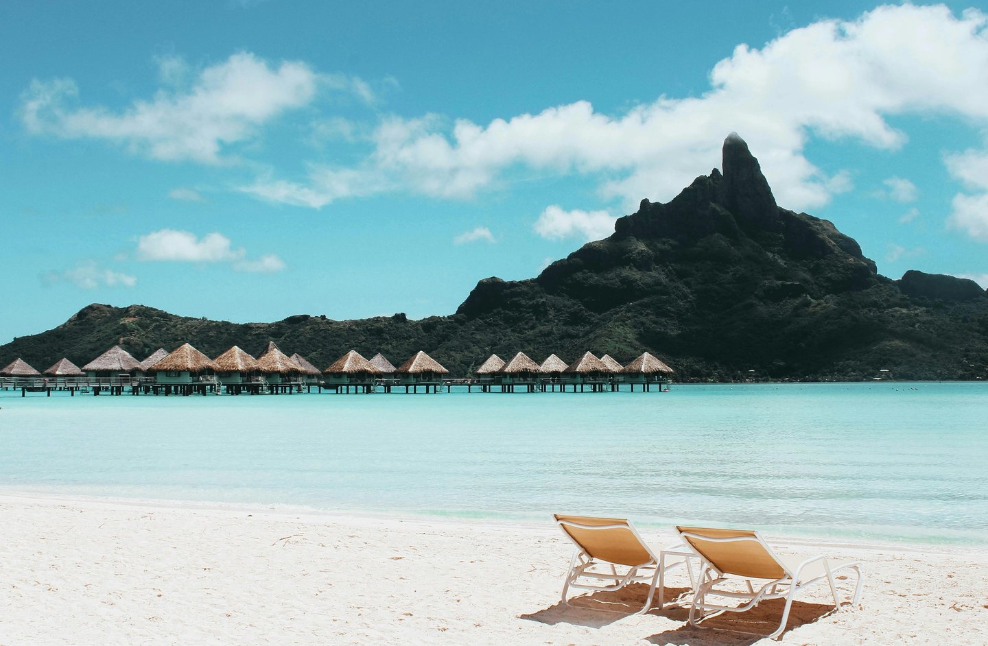 Luxury overwater bungalows in Bora Bora with a sandy beach and Mount Otemanu view.