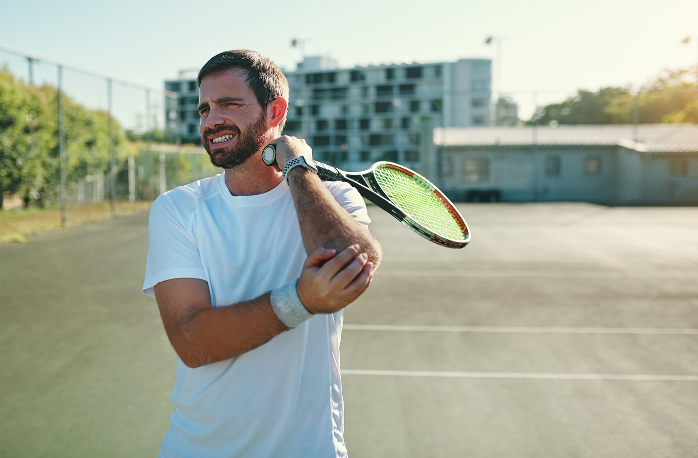 A male tennis player holding his painful elbow, demonstrating a common tennis elbow injury on court.
