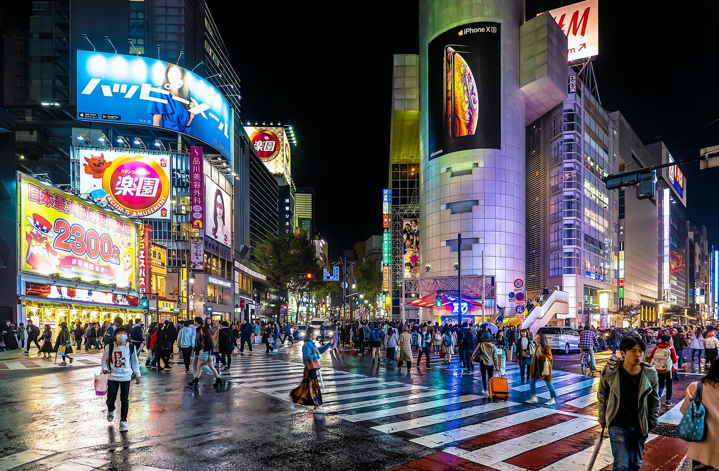 Shibuya Crossing Tokyo at night with illuminated buildings and crowds crossing intersection.