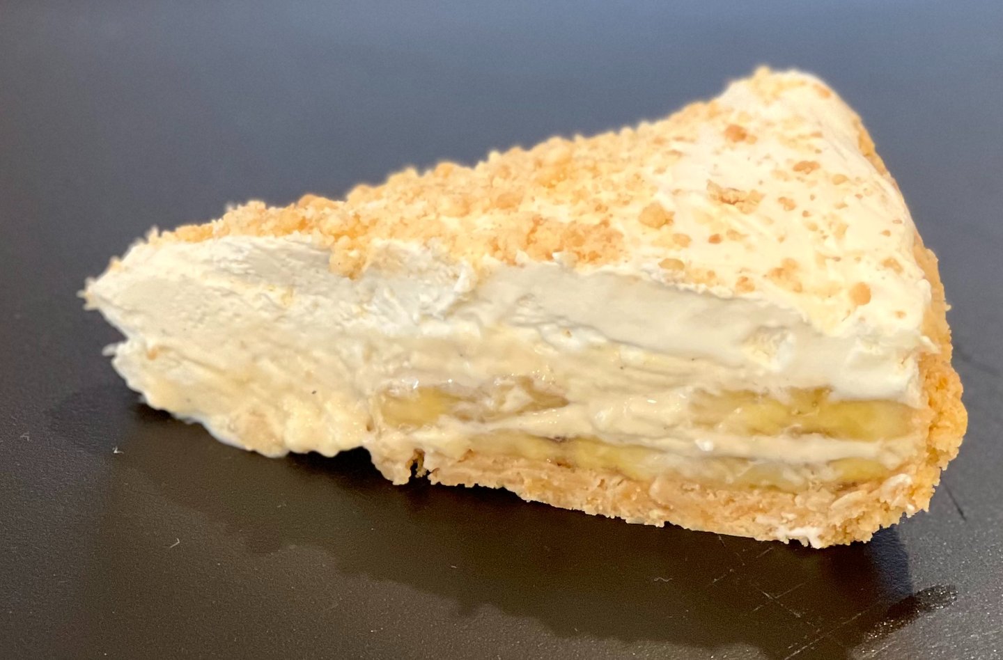 A slice of creamy banana cream pie with a crumbly crust and whipped topping, featuring visible layers of fresh banana and